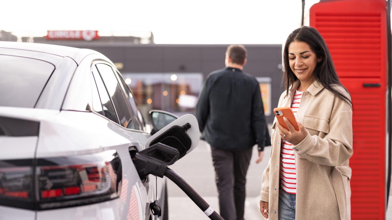 woman happily using her phone while charging her car at Circle K